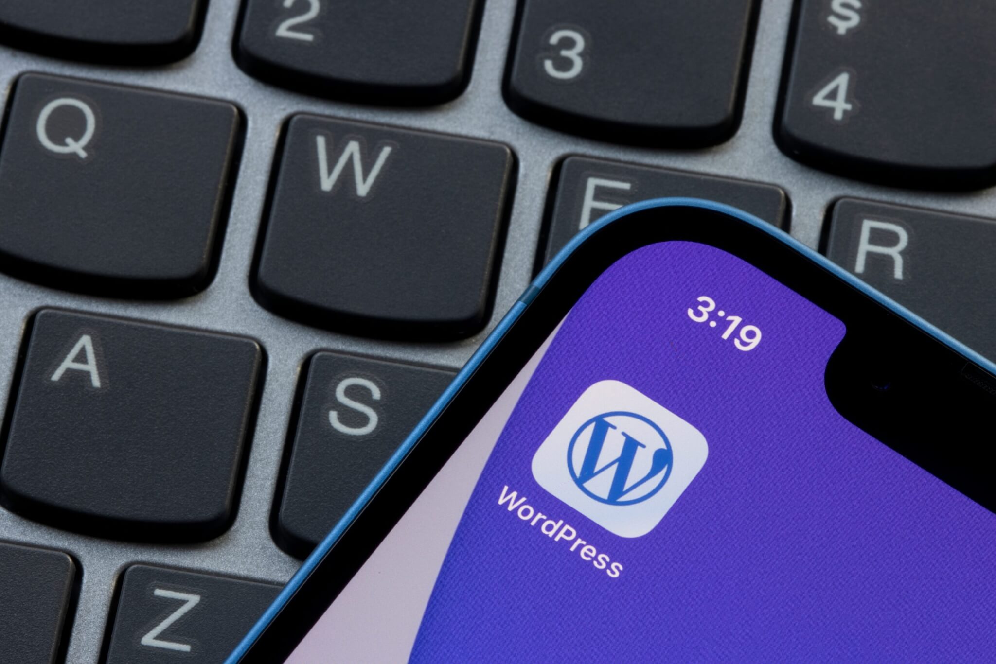 WordPress icon on a mobile phone placed on top of a laptop keyboard.
